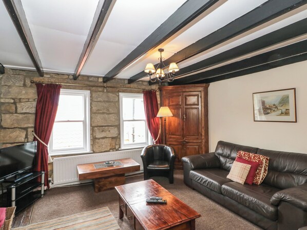 A living room with a stone wall, a wooden cabinet, a leather sofa, a wooden coffee table, and a TV. - Grimes Cottage (Saltburn-by-the-Sea)