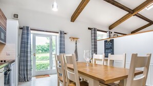 A modern kitchen with a dining area, wooden beams, and a view of the garden. - Teal Barn Annexe (Hereford)