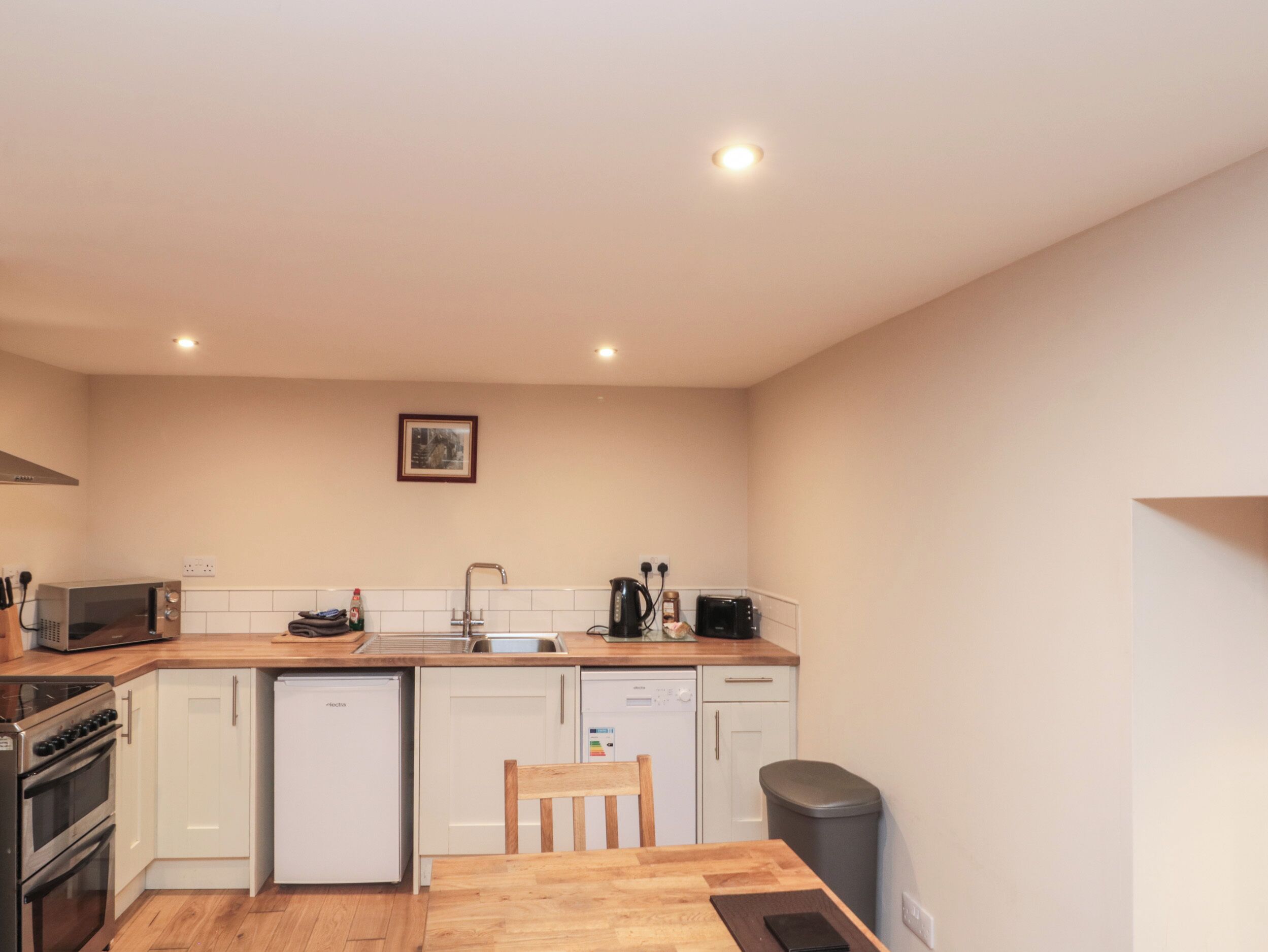 A compact kitchen with white cabinets, a wooden countertop, a sink, a stove, a dishwasher, and a trash bin.