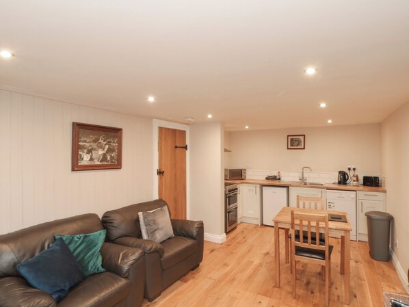 A compact living space with a sofa, a dining table with chairs, a kitchen area with appliances, and a framed picture on the wall. - Grimes Nook (Saltburn-by-the-Sea)