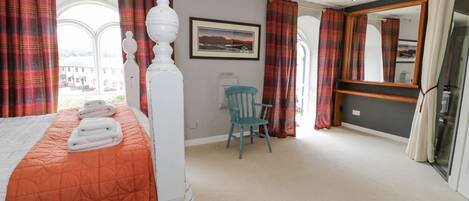 A bedroom with a bed, a chair, a painting, and a large mirror.