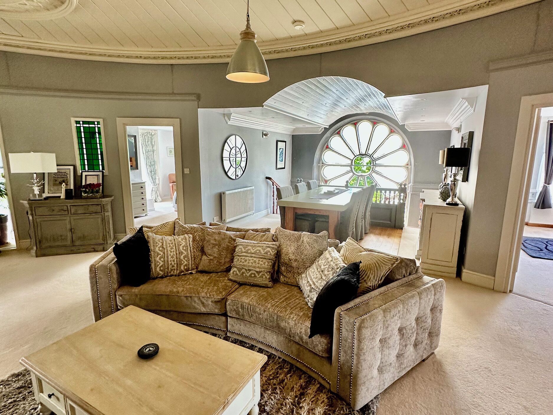 A living room with a sectional sofa, a coffee table, a dining area with a table and chairs, and a large window with a decorative glass design.