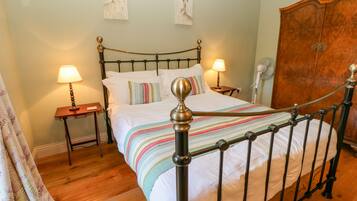 A neatly made bed with a striped blanket, two bedside lamps, and a wooden wardrobe in a room with wooden flooring.