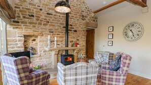 A cozy living room with a stone wall, a fireplace, plaid furniture, and a large clock on the wall. - The Cartshed, Sedbury Park Farm (Richmond)