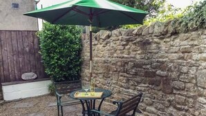 A patio with a stone wall, a wooden fence, and a green umbrella. - The Conifers (Richmond)