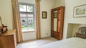A bedroom with a bed, a wooden dresser, a mirror, and a window with curtains. - The Conifers (Richmond)