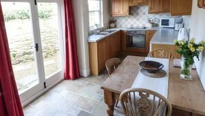 A kitchen with wooden cabinets, a dining table, chairs, a microwave, and a vase with flowers. - The Conifers (Richmond)