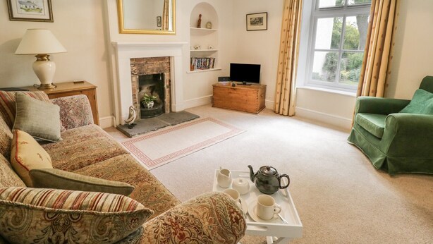 A living room with a sofa, a television, a fireplace, a window with curtains, and a tray with tea set. - The Conifers (Richmond)