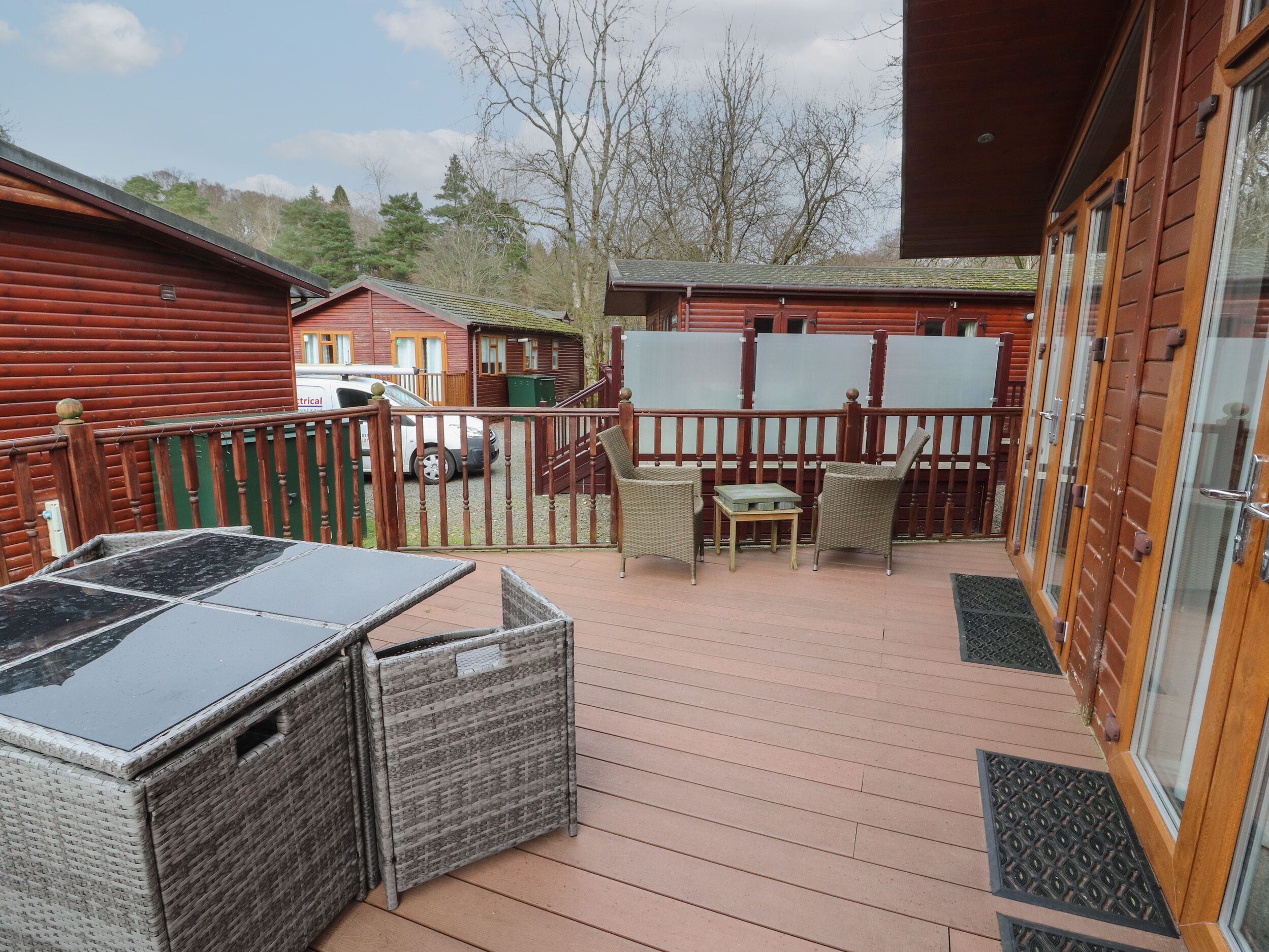 A wooden deck with outdoor furniture, a covered area, and a view of cabins in the background.
