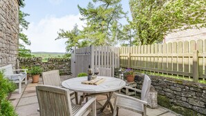 A patio with a round table, wooden chairs, and a stone wall. - Berts Cottage (Appleby-in-Westmorland)