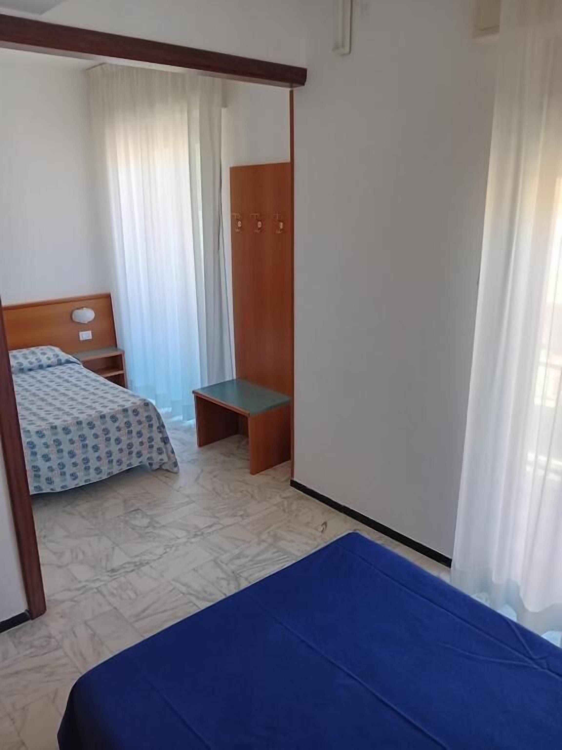 A bedroom with a bed, a wooden wardrobe, a small table, and a bench.