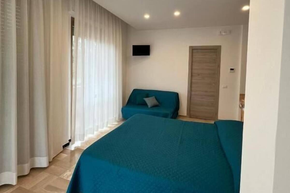Un dormitorio con cama, sofá, televisión y una puerta.