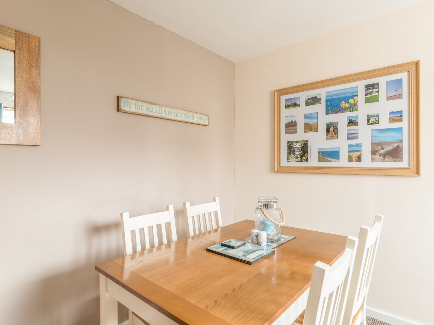 A dining area with a wooden table, white chairs, a framed collage of photos, and a sign on the wall.