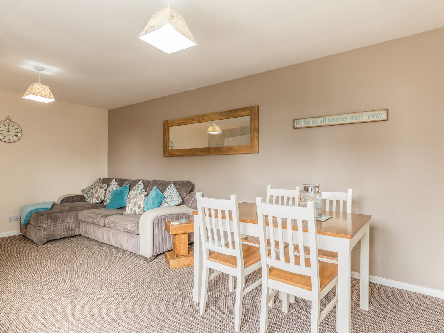 Un salon confortable avec un canapé, une table à manger avec des chaises, une petite table en bois, une horloge et un miroir au mur.