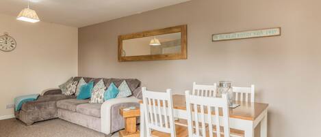 Un salon confortable avec un canapé, une table à manger avec des chaises, une petite table en bois, une horloge et un miroir au mur.
