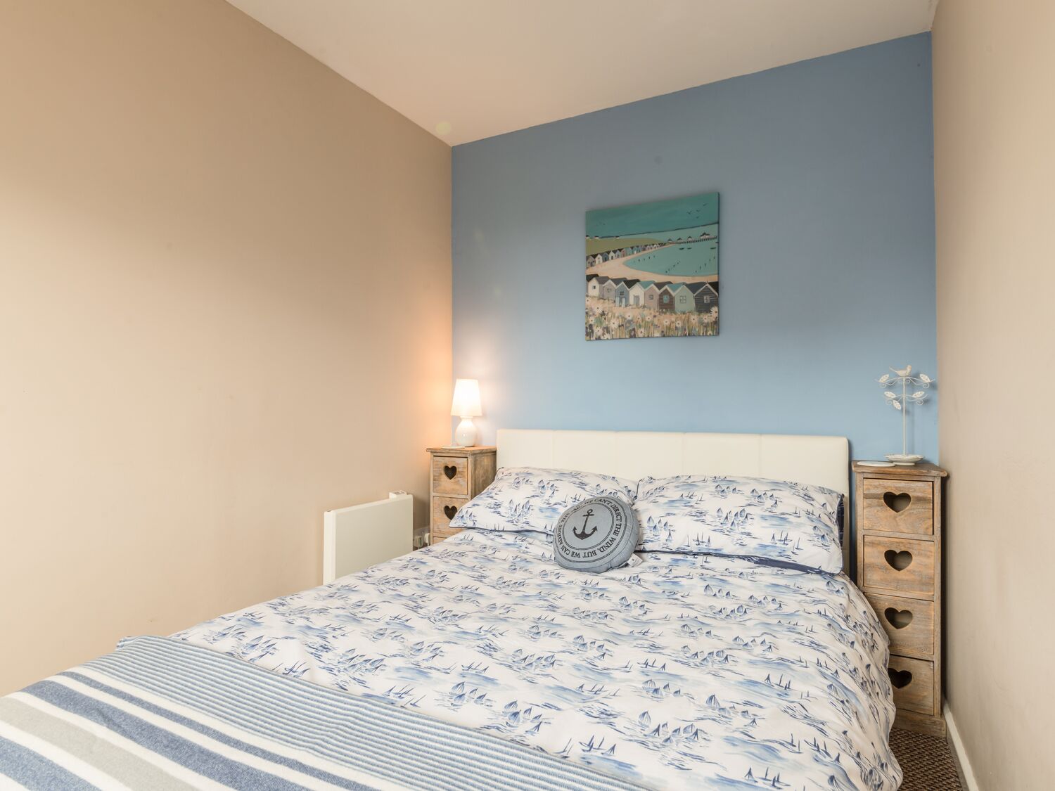 A bedroom with a bed, a nightstand, a lamp, a painting, and a decorative item on the nightstand.