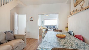 A dining area with a long table, chairs, and a bowl. There is a sofa and a staircase in the background. - 2 Tregof Terrace (Cemaes Bay)