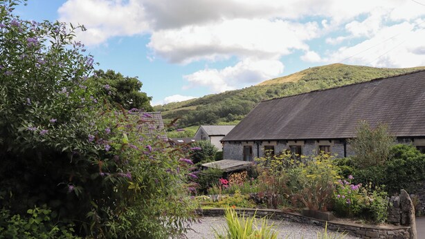 A traditional stone building with a sloped roof, surrounded by lush gardens and a gravel path. - Town End Barn (Hope Valley)