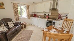 A modern kitchen with white cabinets, a red kettle, and a dining table set for two. - Lawn Lodge (Gloucester)