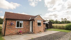 A brick house with a tiled roof, a small porch, and a garden area with flowers and a table. - Lawn Lodge (Gloucester)