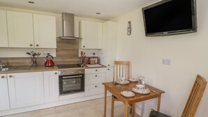 A modern kitchen with white cabinets, a built-in oven, a red kettle, and a dining table set with plates and cups. - Lawn Lodge (Gloucester)