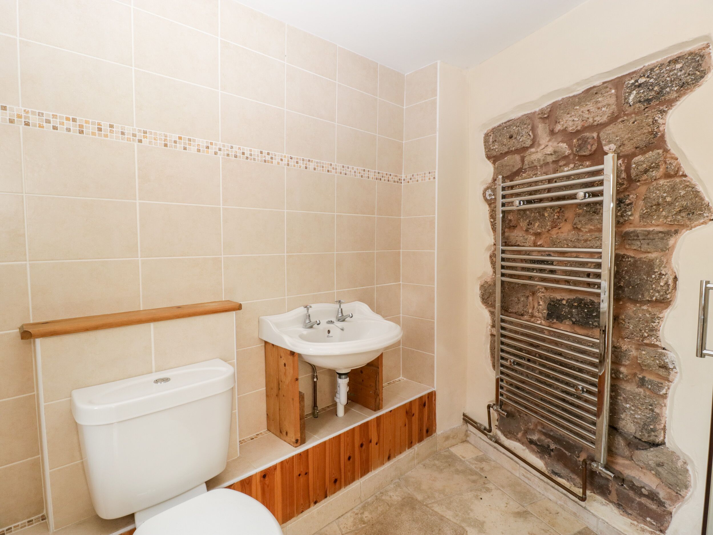 A bathroom with a toilet, sink, and a stone wall with a metal towel rack.