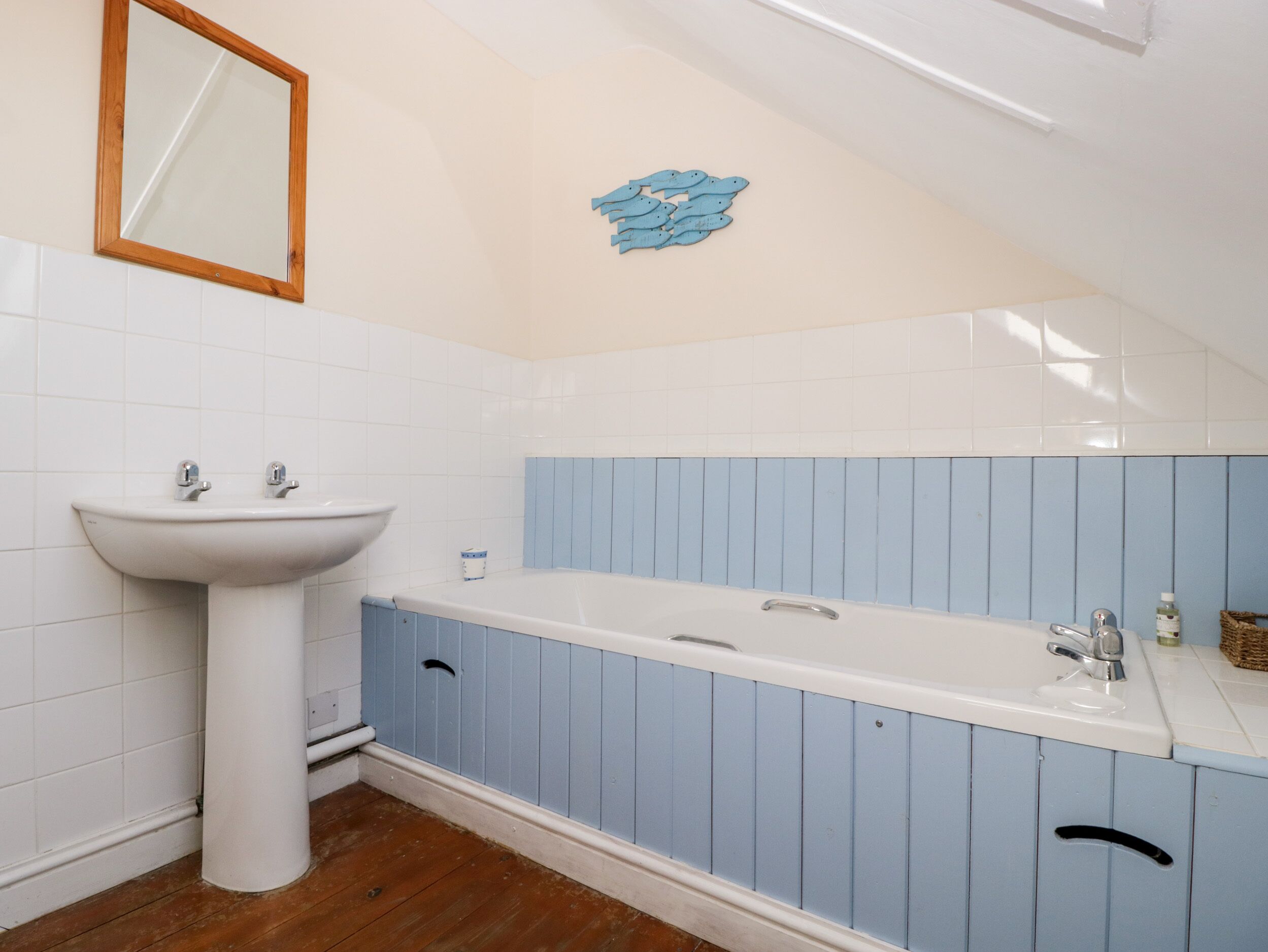 Un baño con un lavamanos pedestal blanco, un espejo grande y un mueble de tocador azul con encimera blanca.
