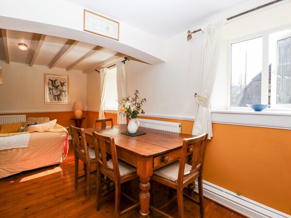 A cozy room with a wooden dining table, chairs, a bed, and a window with curtains. - The Pound (Monmouth)
