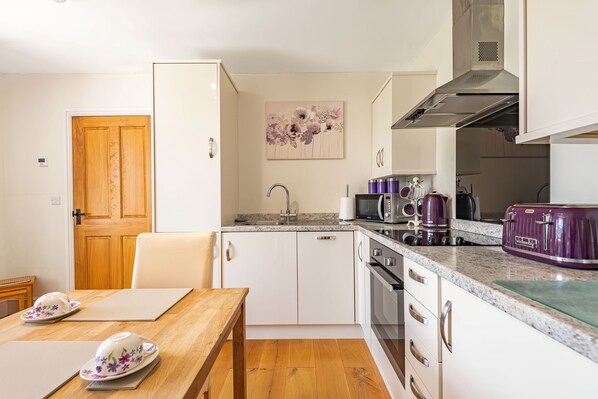 A compact kitchen with white cabinets, a wooden dining table, and a microwave. - Waedog Bach (Bala)