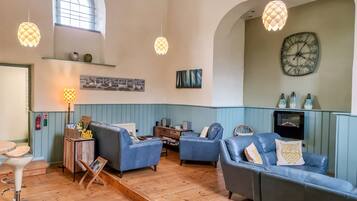 A spacious living room with blue sofas, wooden flooring, and hanging pendant lights.