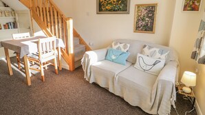 Ein gemütliches Zimmer mit einer Holztreppe, einem Sofa mit gemusterten Kissen und einem Blumenbild an der Wand.
