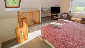 Ein Schlafzimmer mit einer Holztreppe, einem Bett mit floralem Überwurf, einem Fernseher und einem Fenster mit Blick auf Bäume.
