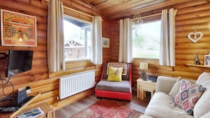 A cozy cabin interior with a wooden interior, a red sofa, a white couch, and a small table with a lamp. - Harbottle Lodge (Morpeth)