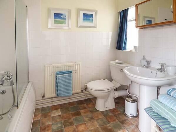 A bathroom with a toilet, sink, and bathtub. There are two framed pictures on the wall and a radiator below the toilet.