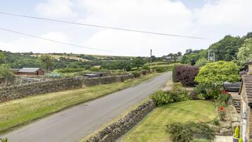 A rural road flanked by stone walls and lush greenery, with houses and a clear sky.