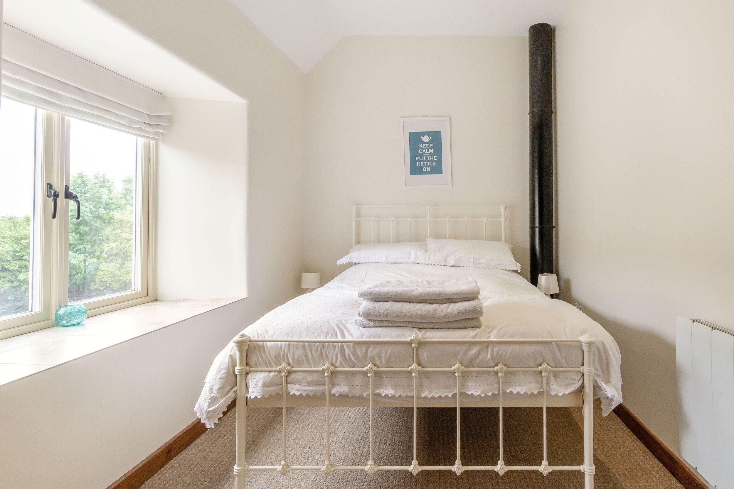 Un dormitorio con cama, ventana, radiador y un póster enmarcado en la pared.