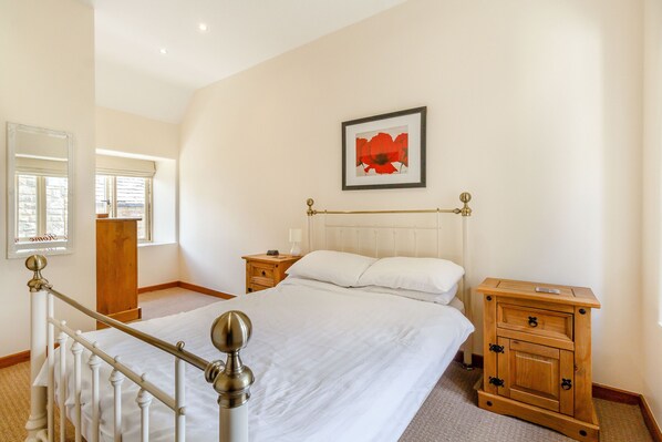Een slaapkamer met een groot bed, houten nachtkastjes, een kapstok, een spiegel en een ingelijste foto aan de muur.