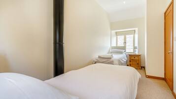 A bedroom with two beds, a wooden wardrobe, a bedside table, and a window with blinds.