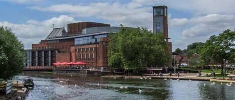 A riverside building with a tower, a bridge, and a walkway with red umbrellas.