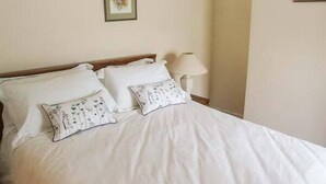 A neatly made bed with white linens and floral-patterned pillows, a wooden headboard, and a bedside lamp. - 11 Victoria Cottages (Stratford-upon-Avon)
