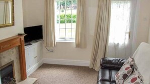A living room with a fireplace, a television, a sofa, and a window with curtains. - 11 Victoria Cottages (Stratford-upon-Avon)