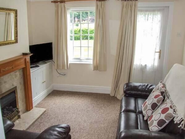 A living room with a fireplace, a television, a sofa, and a window with curtains. - 11 Victoria Cottages (Stratford-upon-Avon)