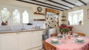 Une cuisine dotée d’un îlot central, de meubles blancs, d’une table à manger recouverte d’une nappe rose et d’une horloge au mur.