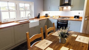 A kitchen with a wooden table, chairs, a sink, cabinets, and a stove. - Little Owl Barn (Buxton)