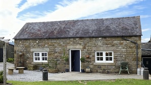A stone building with a dark door, two windows, and a gravel driveway. - Little Owl Barn (Buxton)