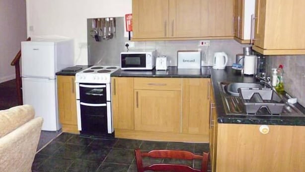 A compact kitchen with wooden cabinets, a stove, a microwave, and a sink. - Harley Apartment (Bishops Castle)