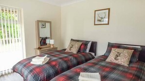 A room with two beds, each with plaid bedding and a deer pillow. There is a mirror on the wall and a framed picture above the beds. - Cwm Gran Meadows (Pontyclun)