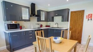 A modern kitchen with dark cabinets, a microwave, and a sink. There is a wooden dining table with chairs and a bowl on it. - Cwm Gran Meadows (Pontyclun)