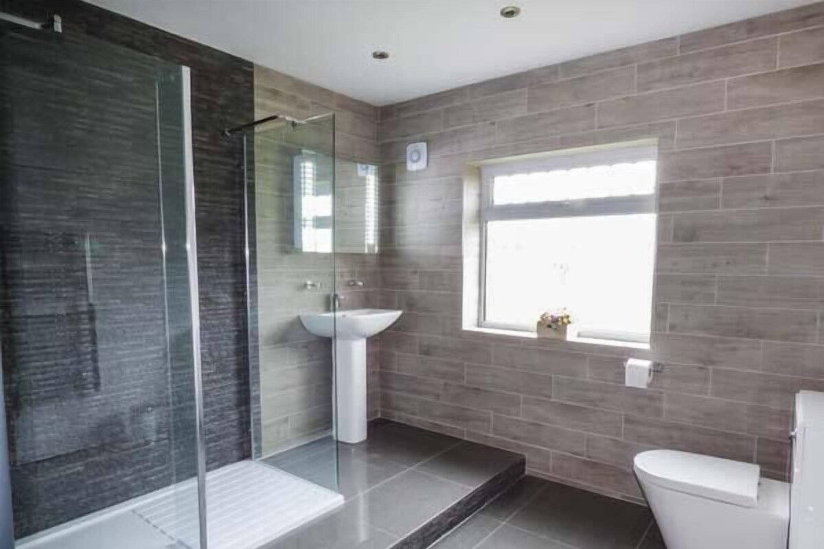 A modern bathroom with a glass shower enclosure, a pedestal sink, and a toilet.