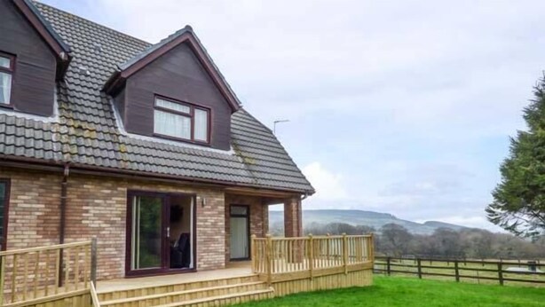 A two-story house with a brick exterior, a tiled roof, and a wooden deck. - Cwm Gran Meadows (Pontyclun)
